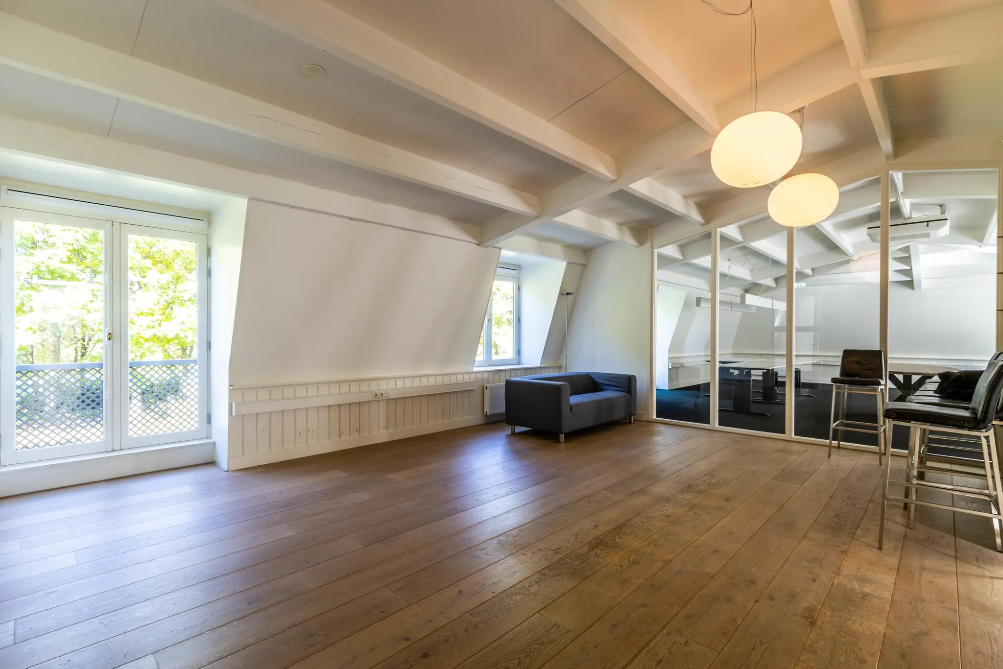 Ruime en lichte zolderkamer aan de Langbroekerdijk met houten vloer, moderne meubels en glazen wand naar vergaderruimte.